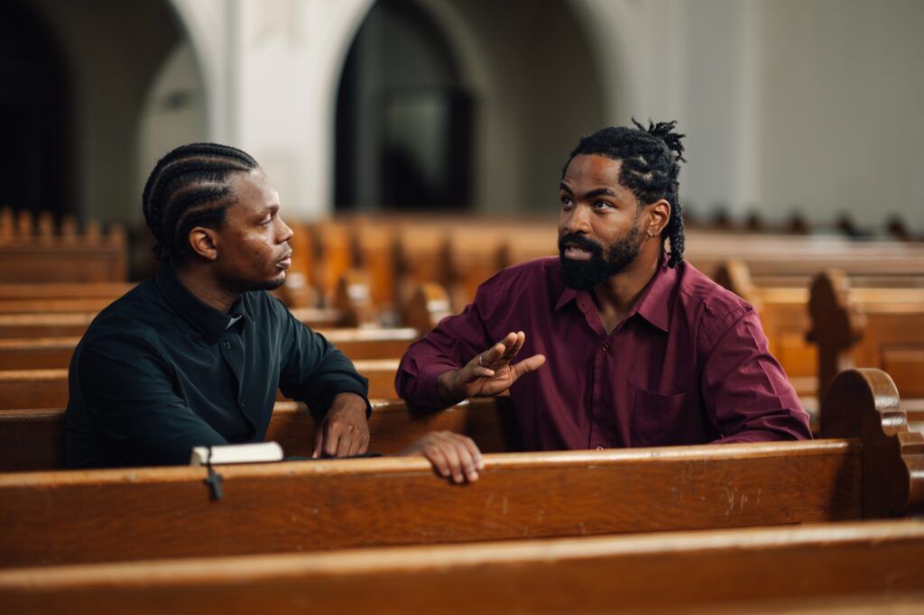 Two men having a serious conversation in church pews
